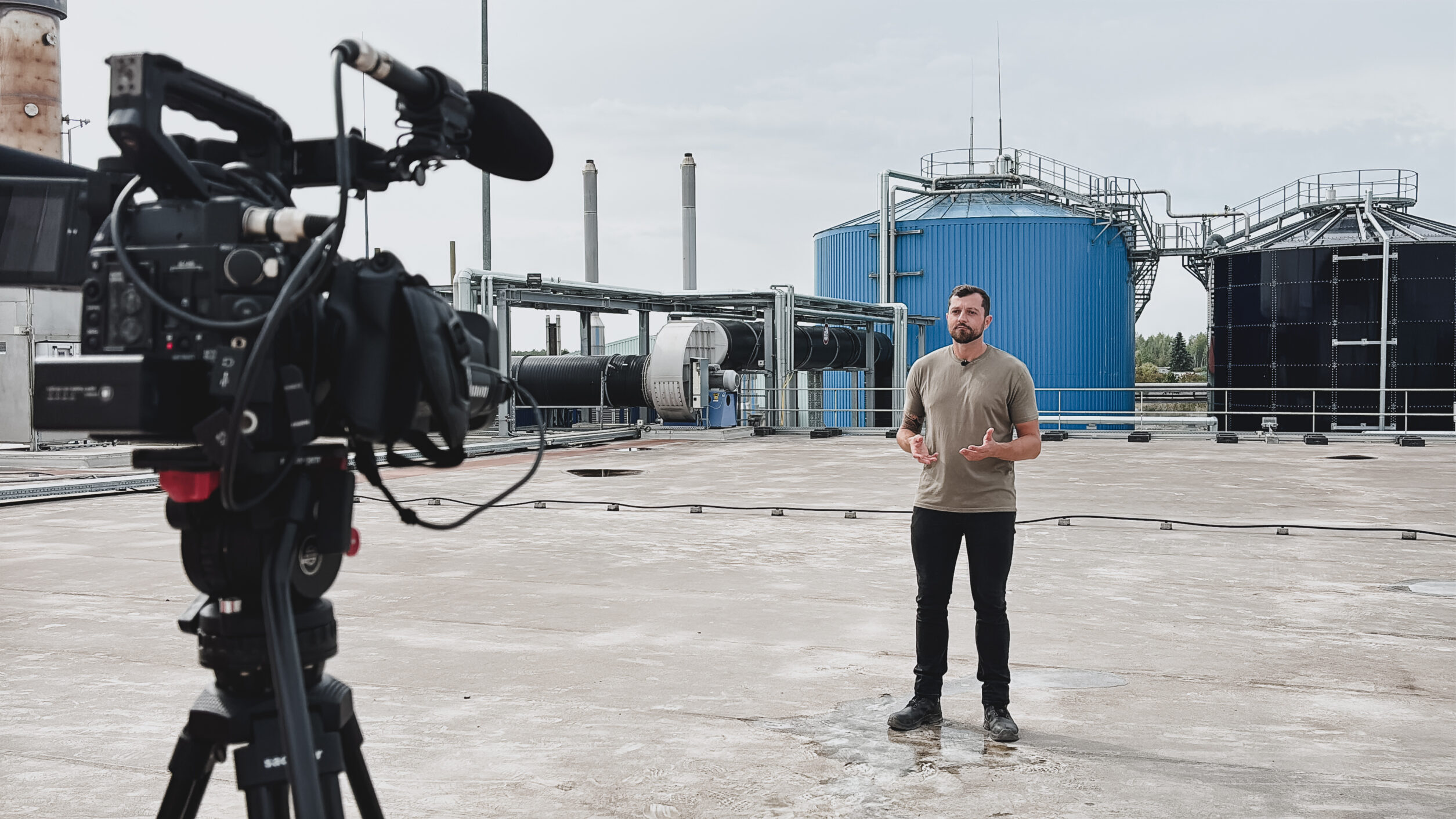 Mann spricht vor Kamera auf Industriedach mit Prozesswassertanks im Hintergrund