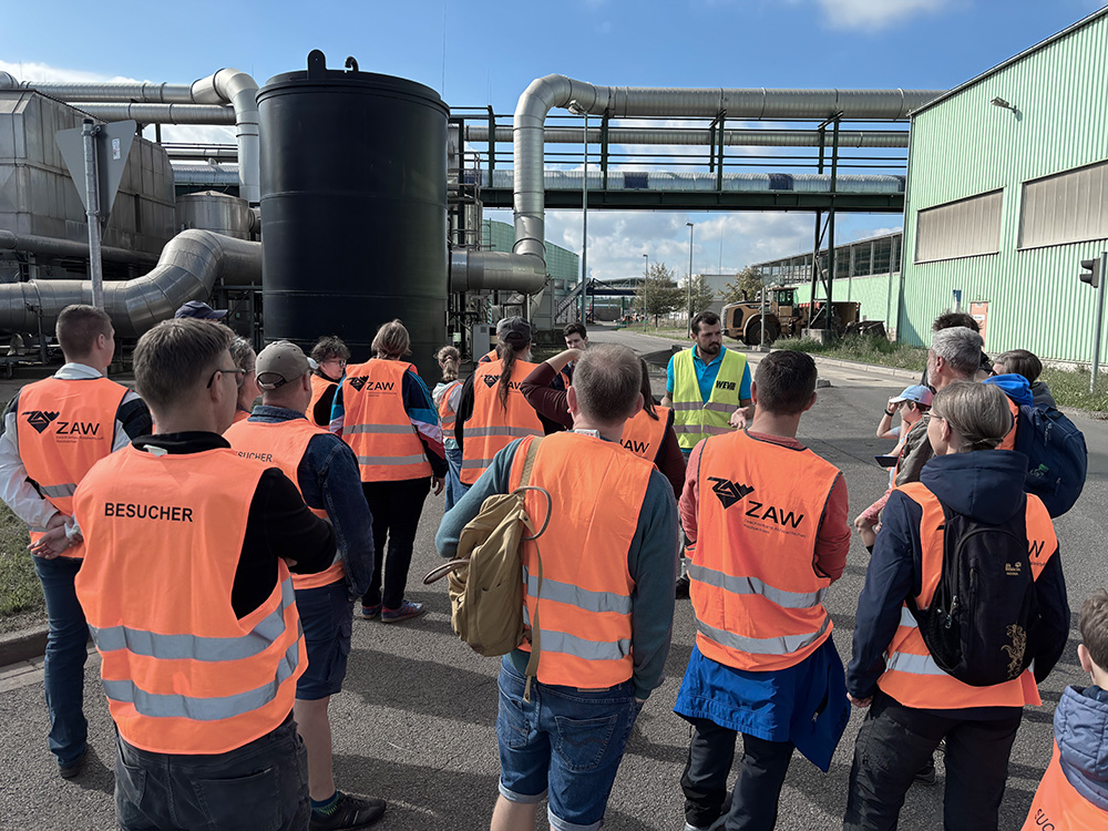 Besuchergruppe in Warnwesten vor Industrieanlage mit Rohren